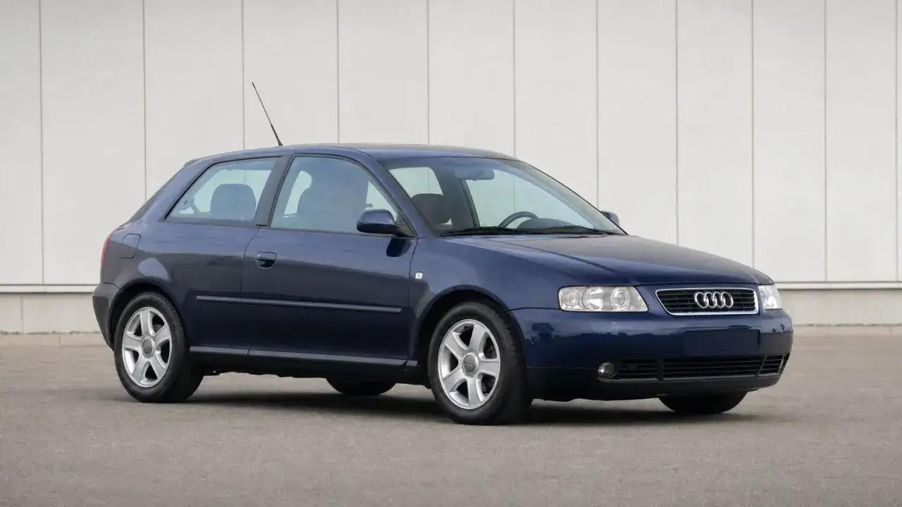 Dunkelblauer Audi A3 Baujahr 2000, dreit&uuml;rig, steht auf einem Parkplatz vor einer hellen Wand.