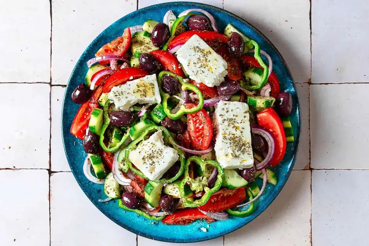 Frischer Feta Salat mit Tomaten, Gurken, Paprika, roten Zwiebeln und Kalamata-Oliven, garniert mit Kräutern.