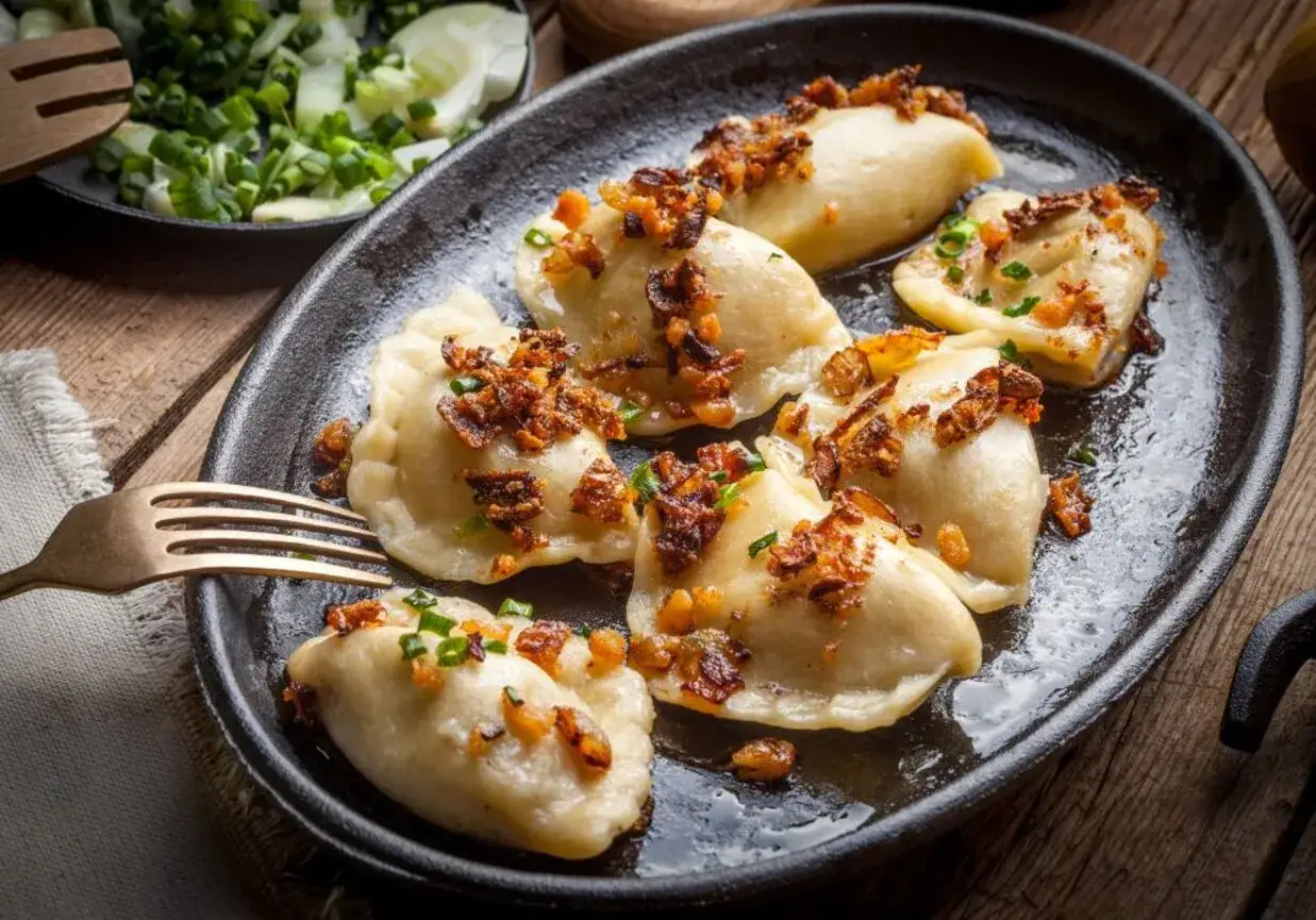 Pyszne pierogi z mięsem mielonym surowym, posypane skwarkami i szczypiorkiem, czekają na widelcu. Obok surówka z kapusty.