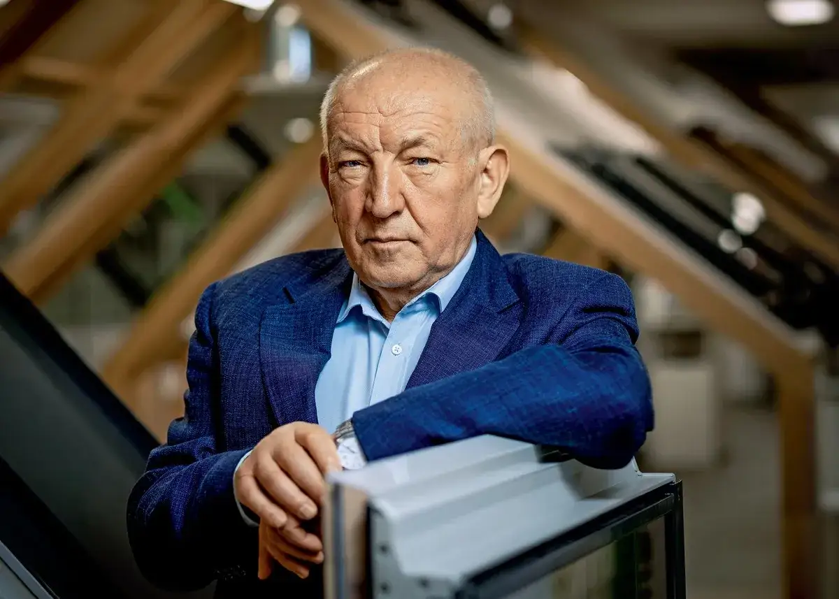Starszy mężczyzna w garniturze, właściciel firmy, opiera się o ramę okna.