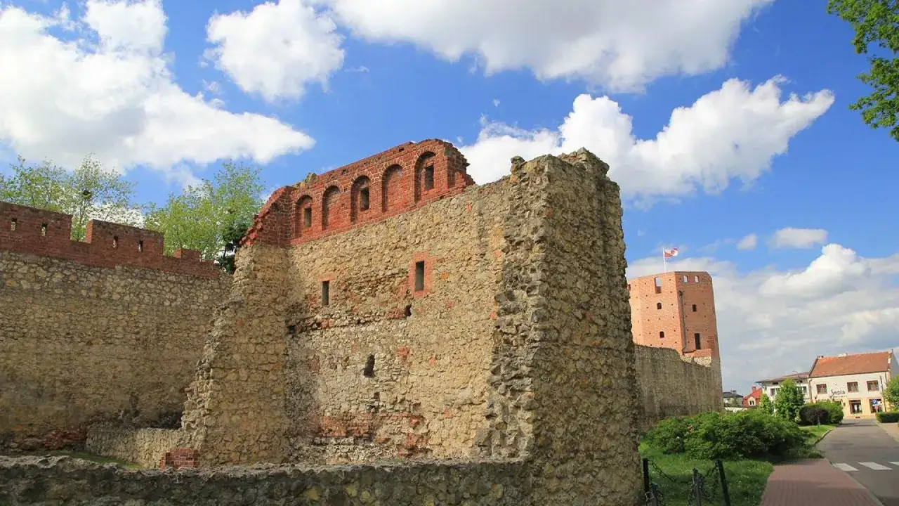 Kamienne ruiny zamku, przypominające polskie Carcassonne, z ceglaną wieżą i błękitnym niebem.