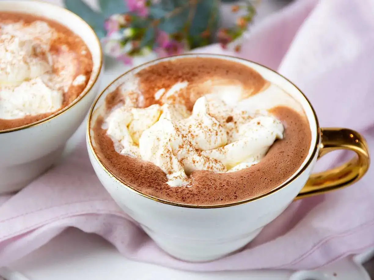 Två muggar med krämig varm choklad, toppad med vispad grädde och kanel. Perfekt för en mysig stund.