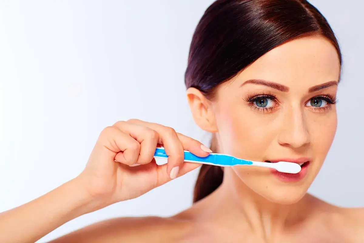 Mujer con cepillo de dientes azul y blanco, quiz&aacute;s cometiendo errores al cepillarse los dientes.