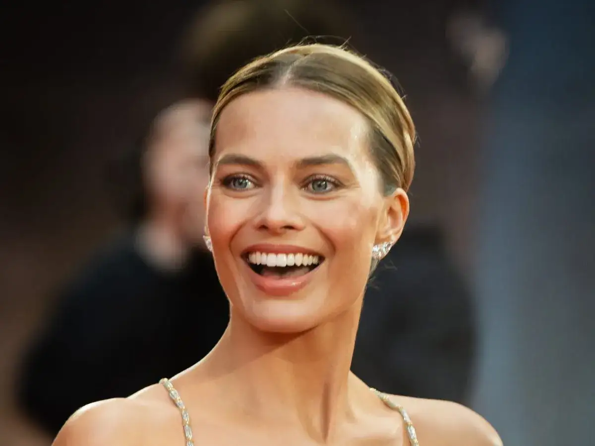 Uśmiechnięta Margot Robbie bez makijażu, z błyszczącymi kolczykami, wygląda naturalnie i promiennie.