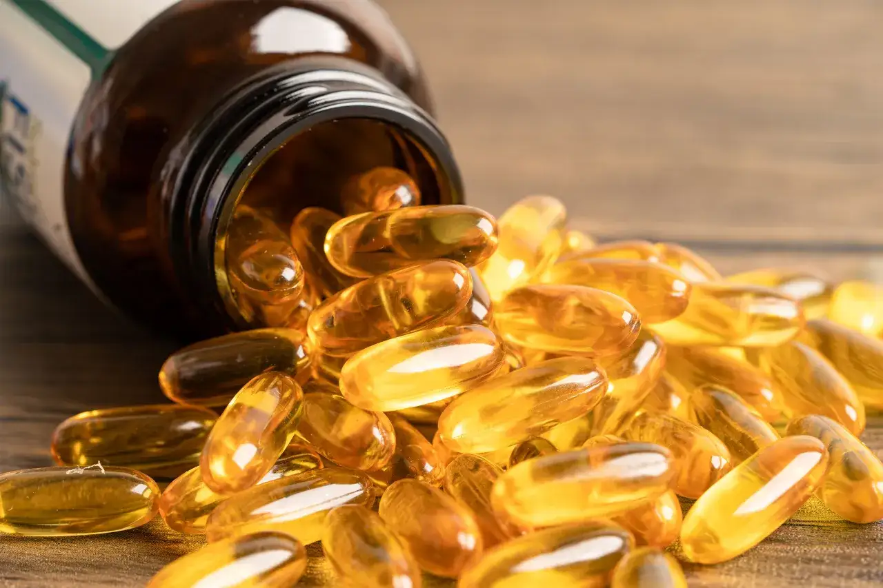 Ż&oacute;łte kapsułki omega-3 wysypują się z brązowej butelki. Dowiedz się, z czym nie łączyć omega-3, by uniknąć interakcji.