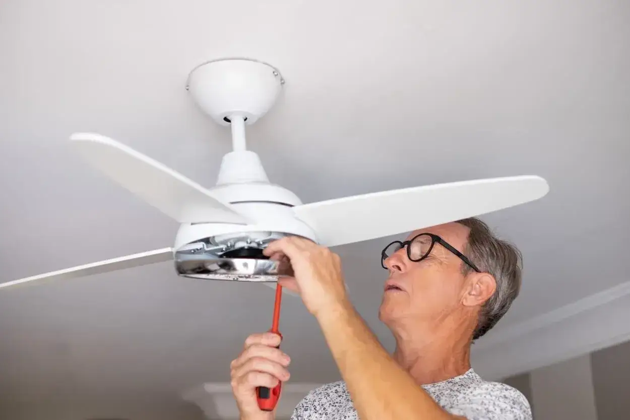 Hombre con gafas ajusta un ventilador de techo pladur con un destornillador.