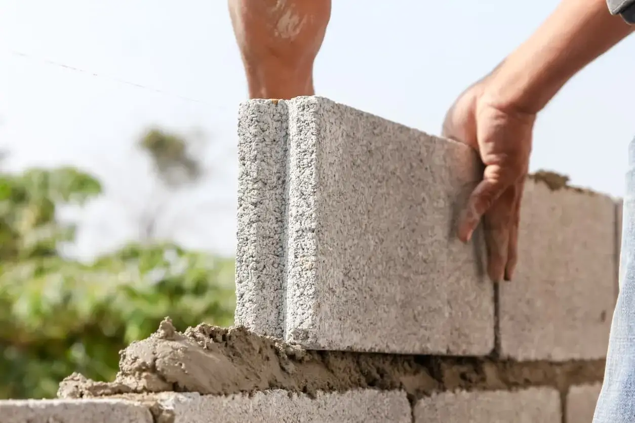 Manos colocan un bloque de cemento para construir una pared de bloques.