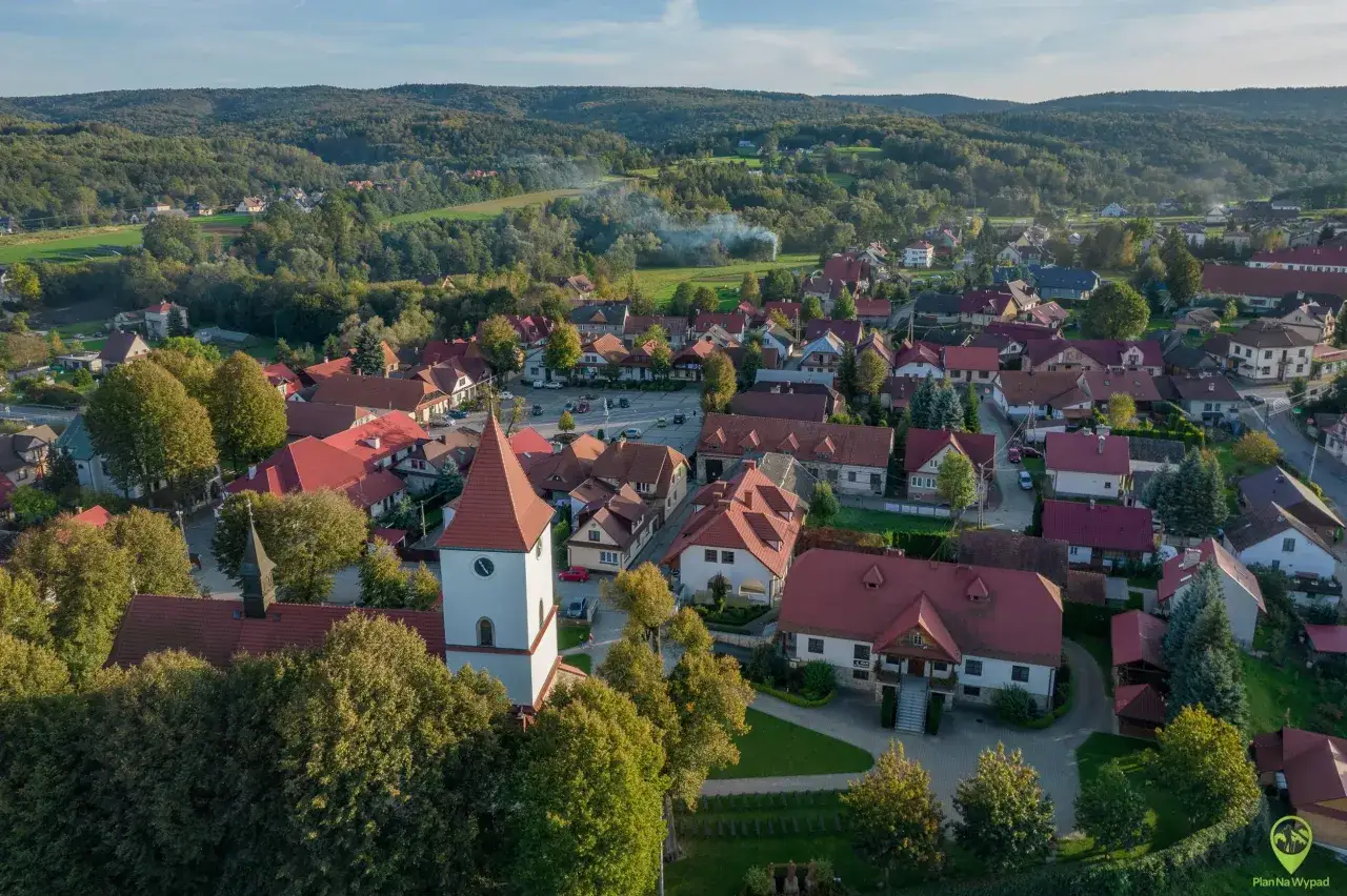 Widok z lotu ptaka na Lipnicę Murowaną, gdzie widać kościół z wieżą, domy z czerwonymi dachami i otaczające lasy. Odkryj lipnica murowana atrakcje!