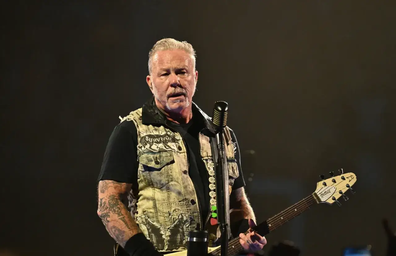James Hetfield, wokalista zespołu Metallica, na scenie z gitarą i mikrofonem.