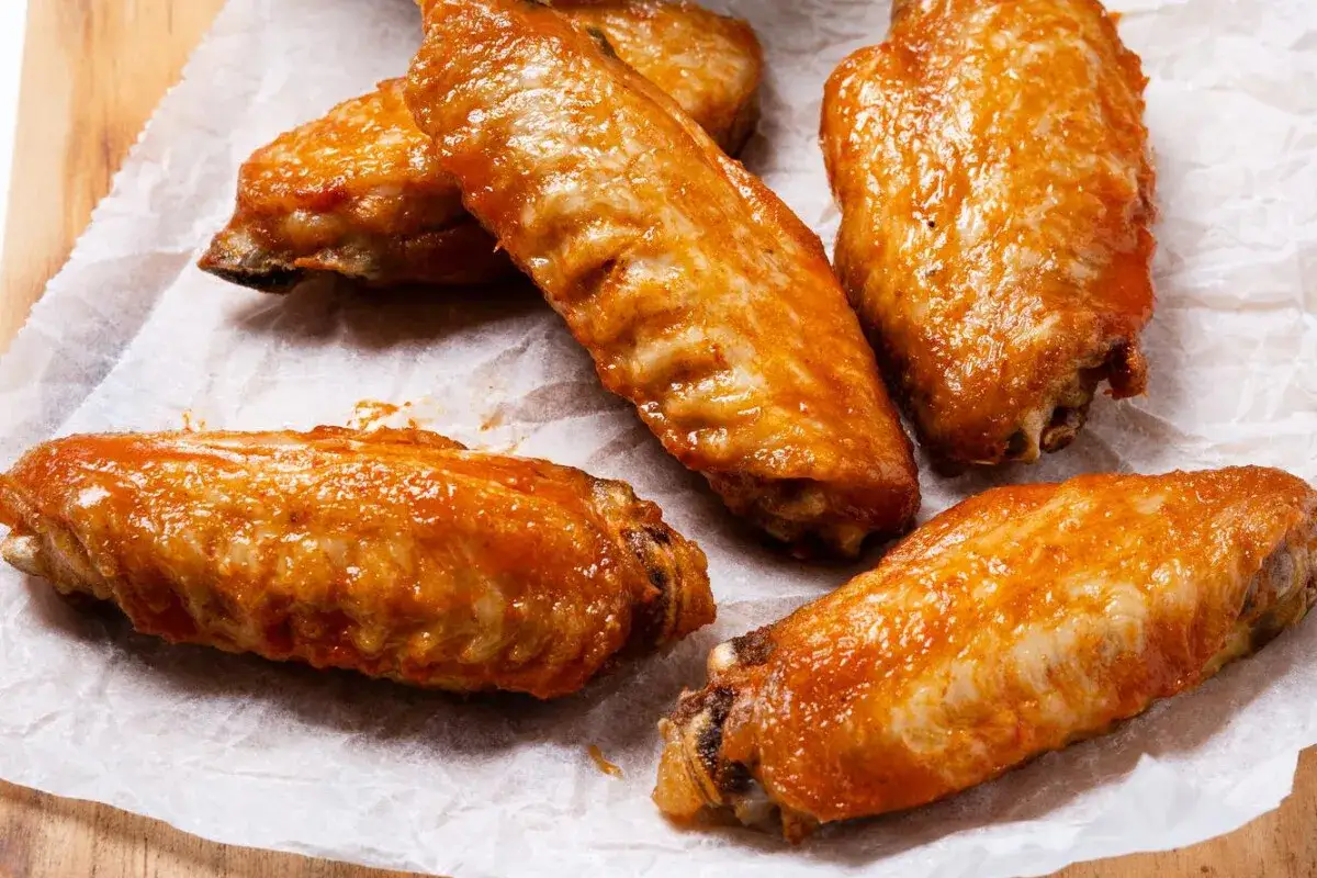 Cinco alitas de pollo al ajillo, doradas y jugosas, servidas sobre papel encerado.
