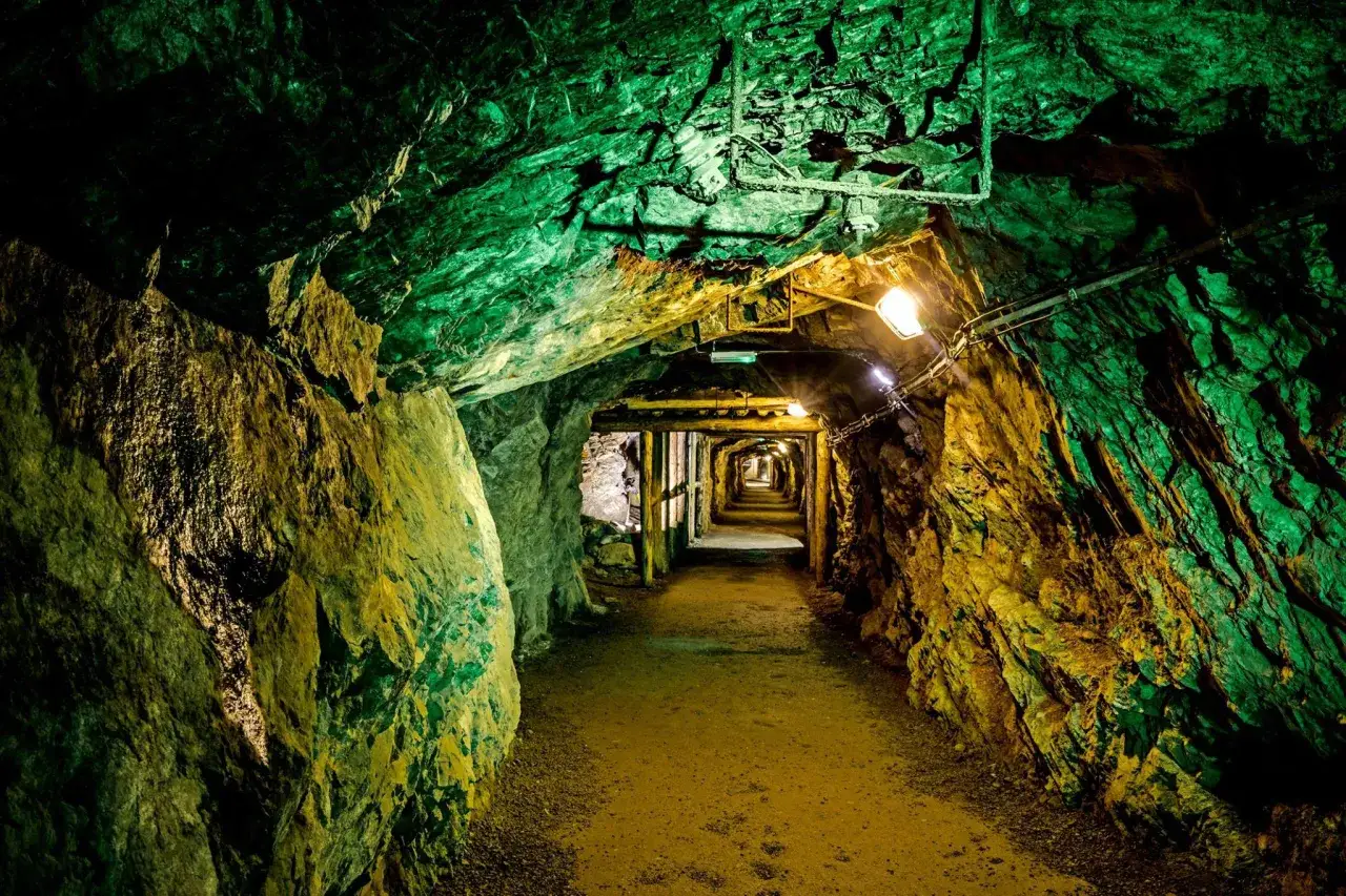 Wydobycie w jaskiniach Dolny Śląsk. Tunel kopalni oświetlony zielonym i żółtym światłem, prowadzący w głąb ziemi.