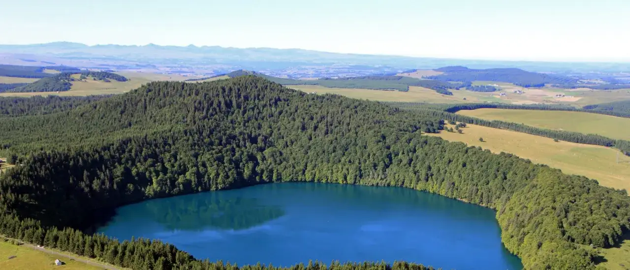 Lac d'un bleu profond entouré de forêts verdoyantes, un paysage magnifique à découvrir si vous cherchez que visiter en Auvergne.