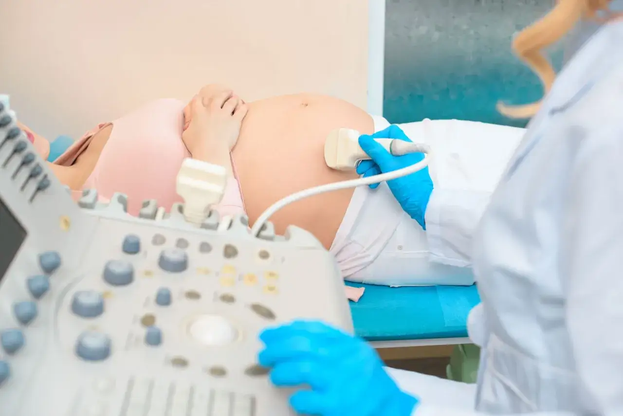 Lekarz wykonuje badanie prenatalne, przykładając głowicę USG do brzucha ciężarnej kobiety.