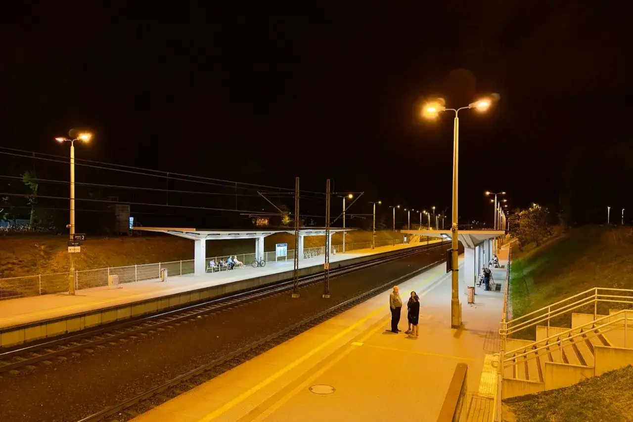 Nocny dworzec kolejowy, ludzie czekają na pociąg. Sprawdzają nowy rozkład jazdy Sandomierz.