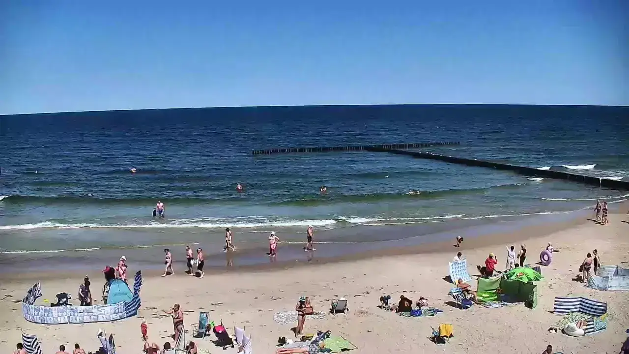 Słoneczna plaża w Dźwirzynie, ludzie kąpią się w morzu i odpoczywają na piasku. Wiele atrakcji dla turystów.