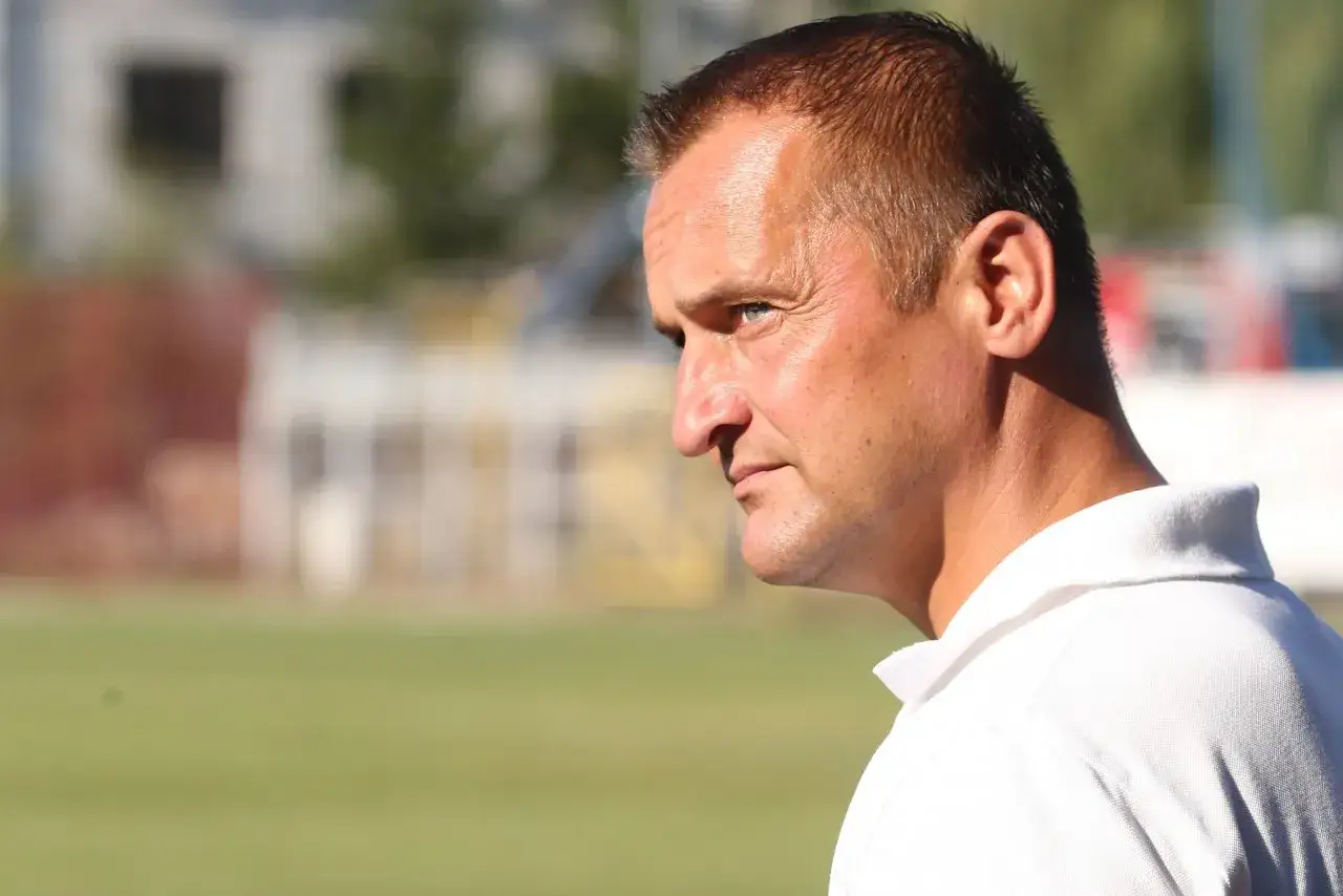 Dariusz Dźwigała w białej koszulce polo, zamyślony, na tle boiska.