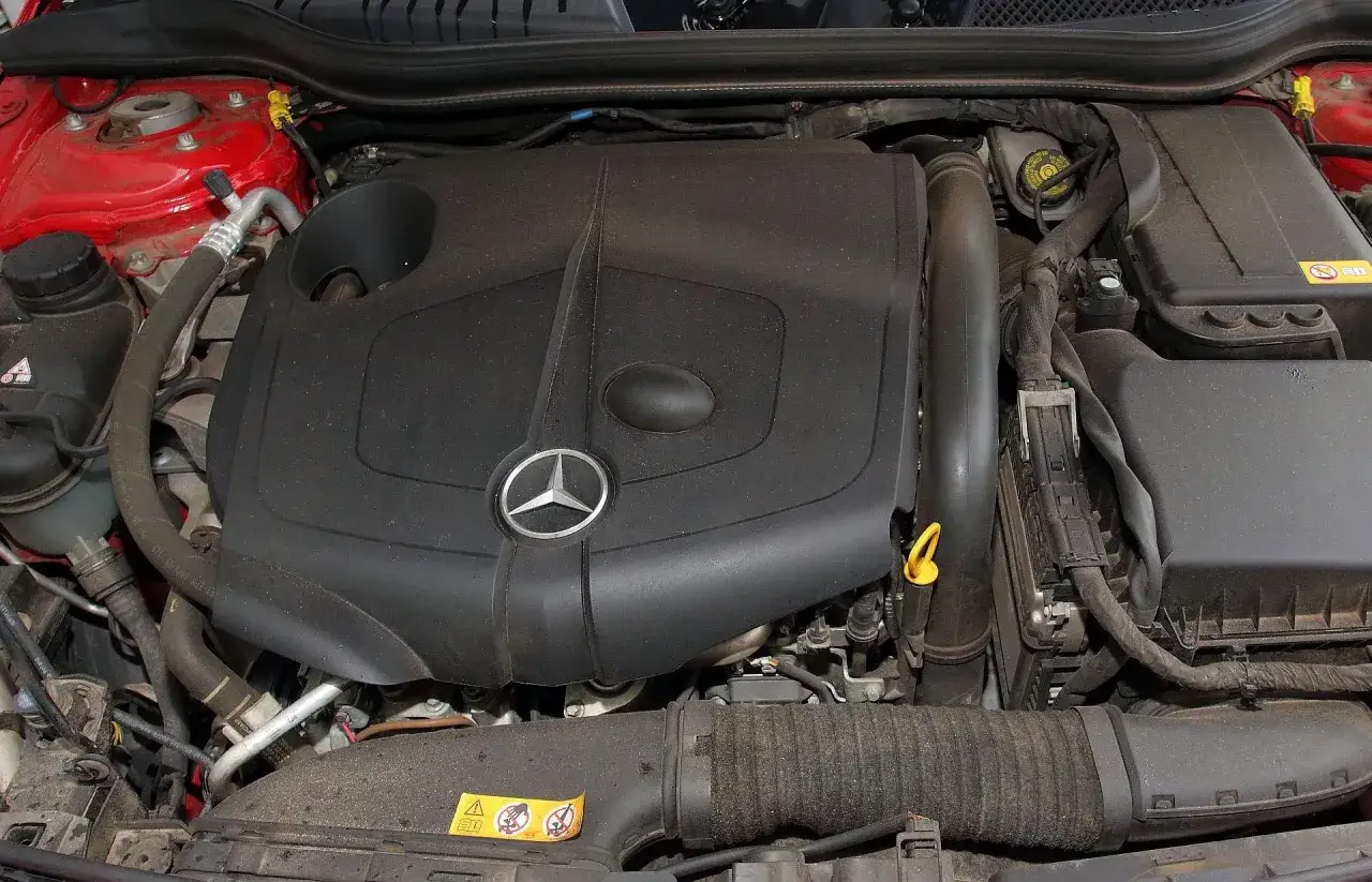 Silnik Mercedesa W176, widoczny pod maską, z charakterystyczną osłoną i logo gwiazdy.