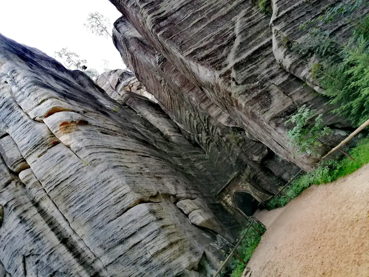 Wąska ścieżka prowadzi do tunelu wykutego w skalnym mieście w Polsce. Monumentalne, warstwowe skały otaczają drogę.