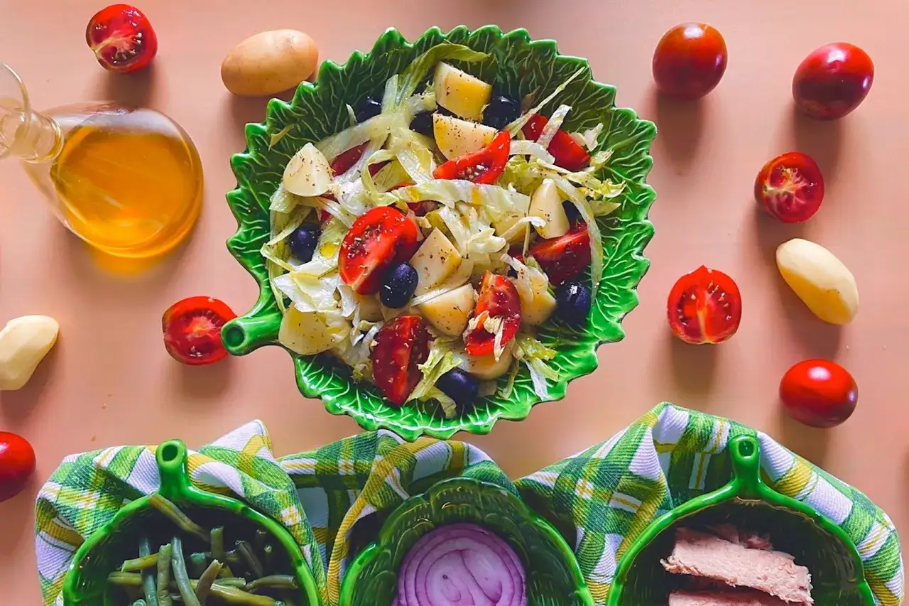 Insalata di patate napoletana con pomodorini, olive e lattuga, condita con olio d'oliva. Ingredienti freschi disposti attorno al piatto.