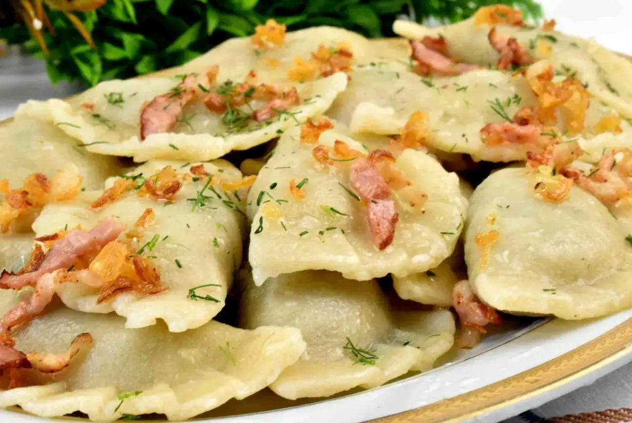 Pyszne pierogi z młodej kapusty, posypane skwarkami i koperkiem, ułożone na talerzu.