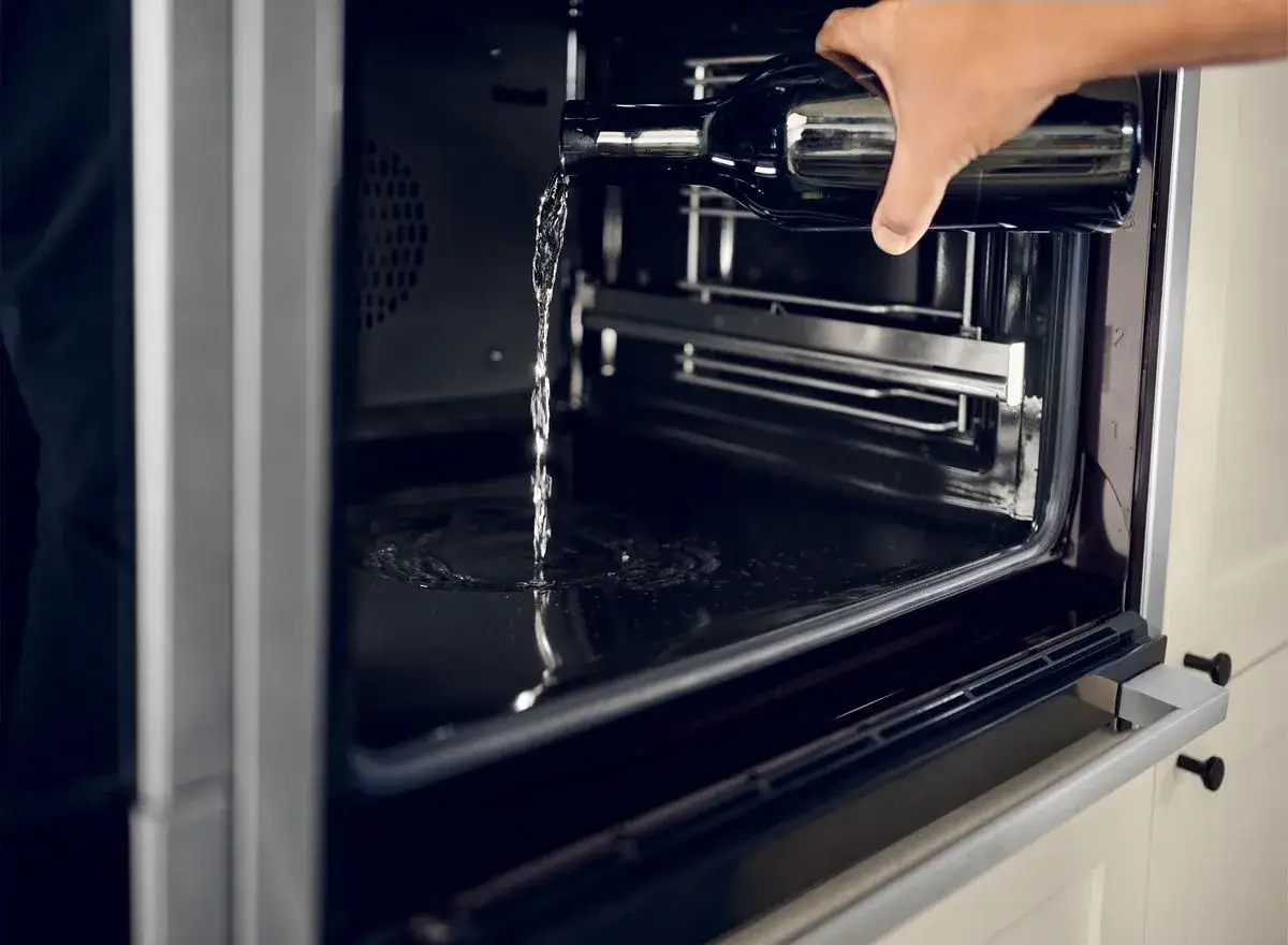 Wasser wird aus einer Flasche in einen modernen hydrolyse backofen gegossen, um die Reinigung zu erleichtern.