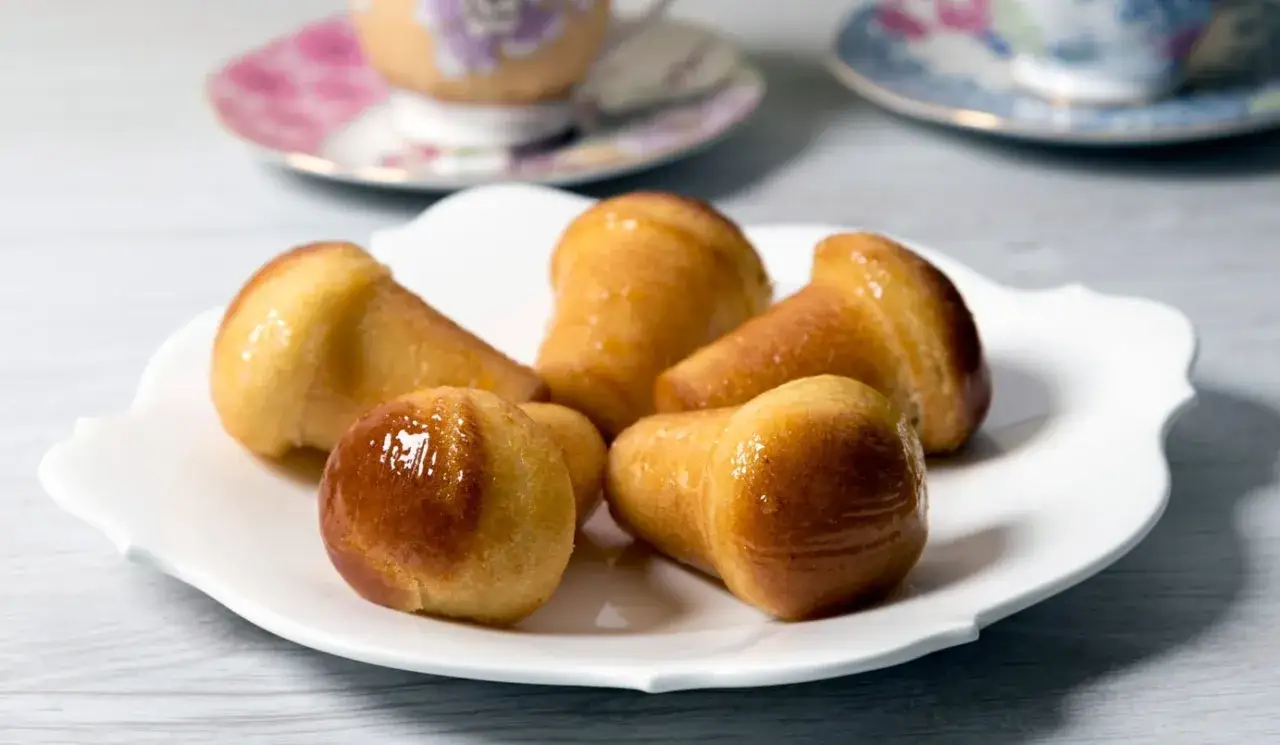 Cinque babà dorati e lucidi su un piatto bianco, pronti per essere gustati con un caffè.