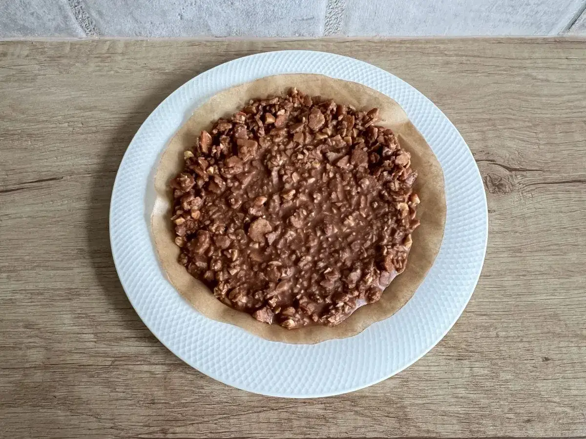 Chrupka czekoladowa do tortu, z orzechami, na papierze do pieczenia, na białym talerzu.