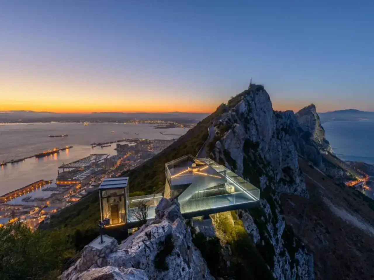 Atardecer sobre el Peñón de Gibraltar, con el Skywalk iluminado y la ciudad extendiéndose hacia el mar.