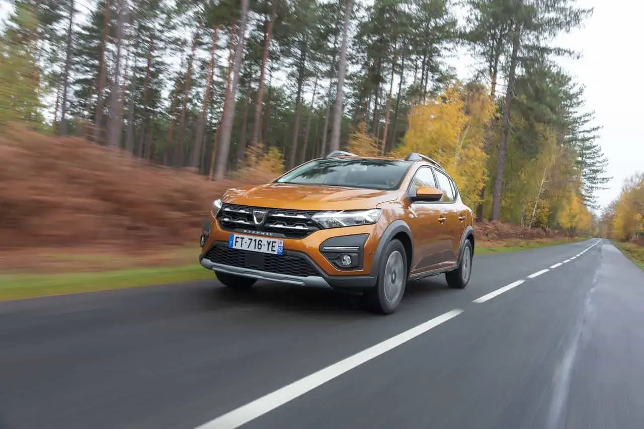 Pomarańczowy Dacia Sandero Stepway pokonuje leśną drogę jesienią, demonstrując swój imponujący prześwit.