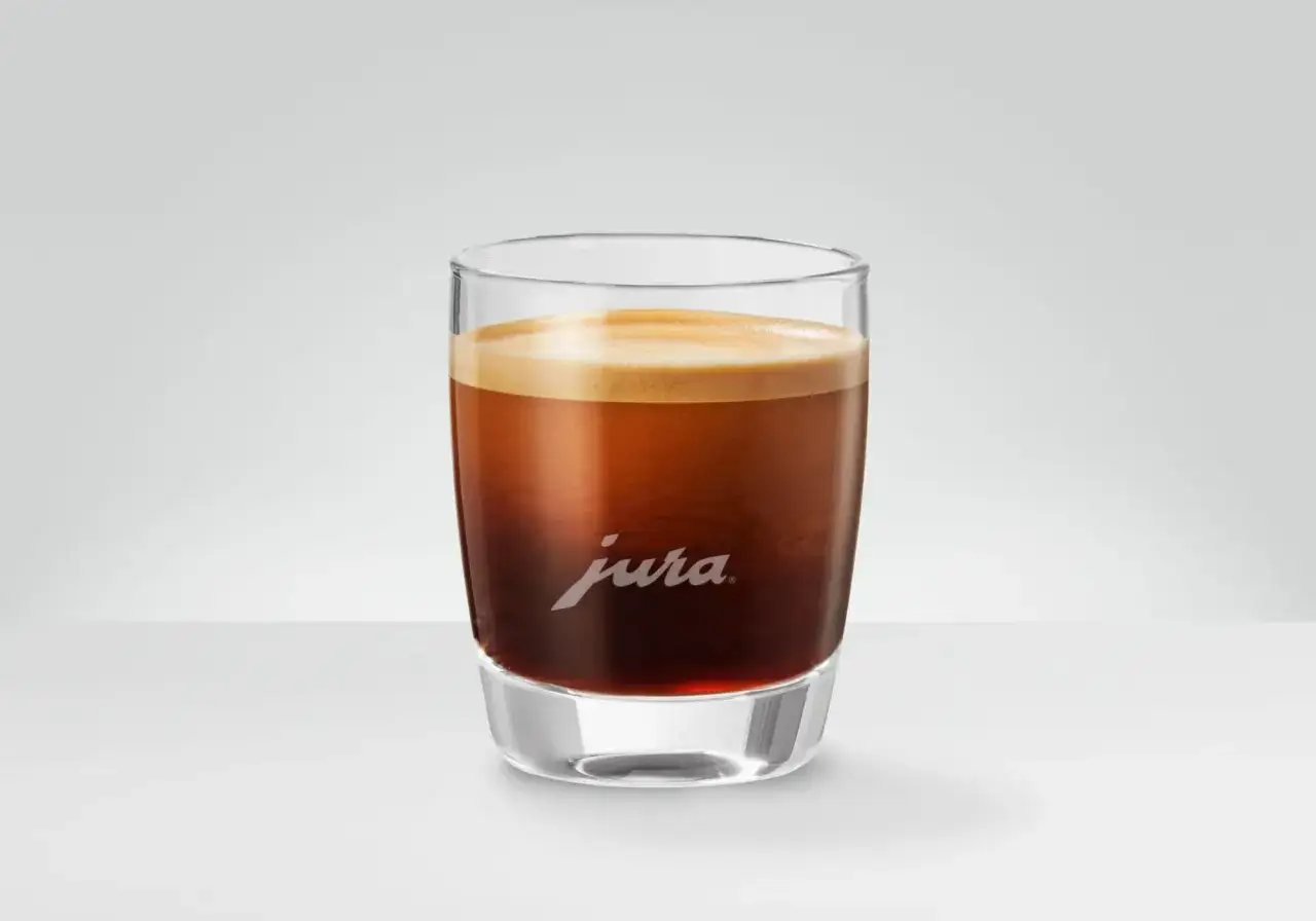 Aromatyczna kawa doppio z gęstą cremą w szklance z logo Jura. Idealny początek dnia.