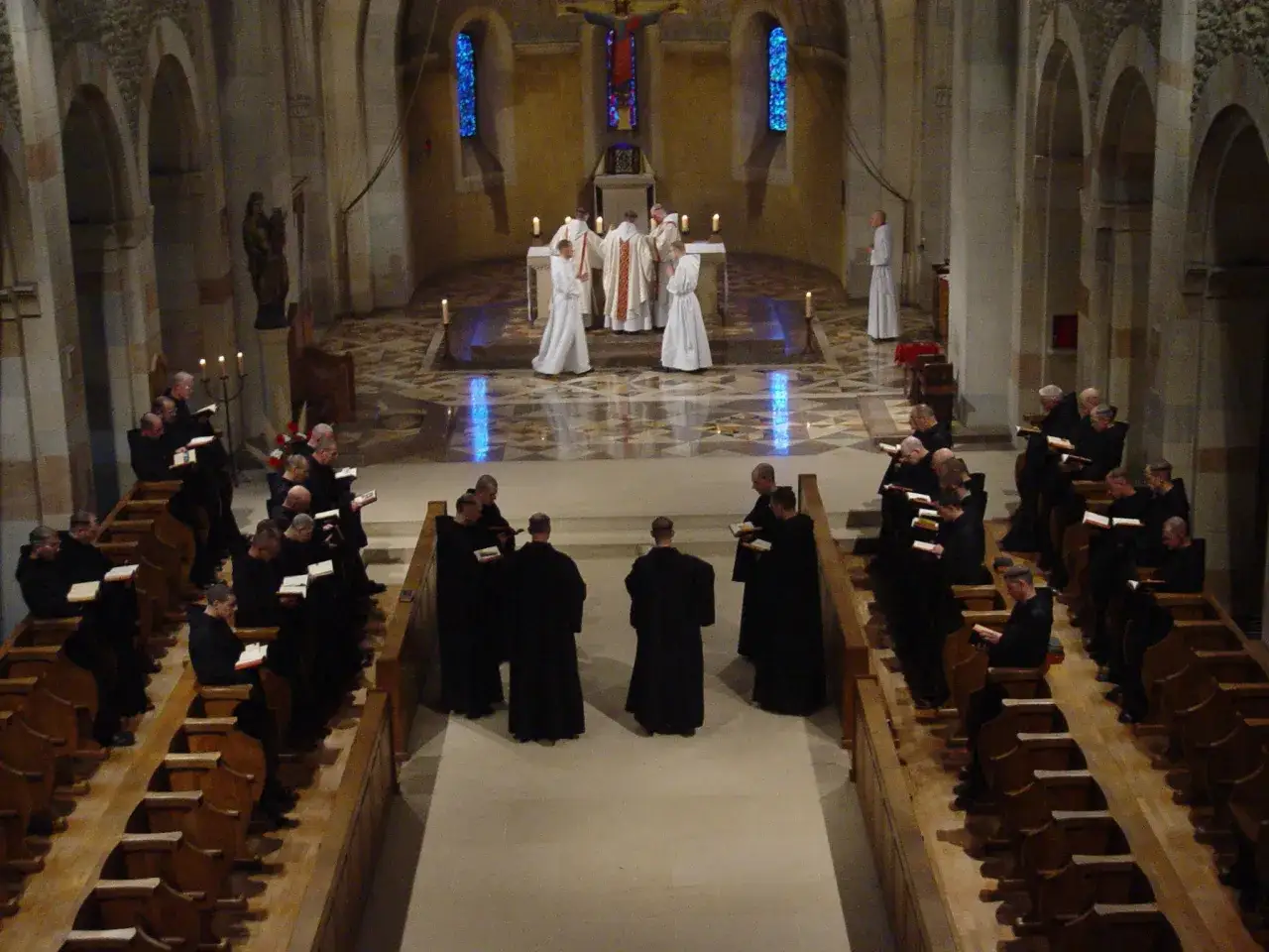 Monks in a church, attending mass. The abbey mass schedule is being followed as they gather for the service.