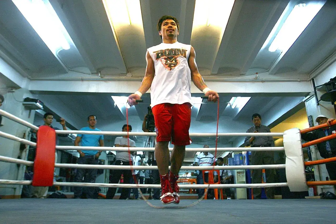 A boxer skip rope in a boxing ring, with spectators watching.