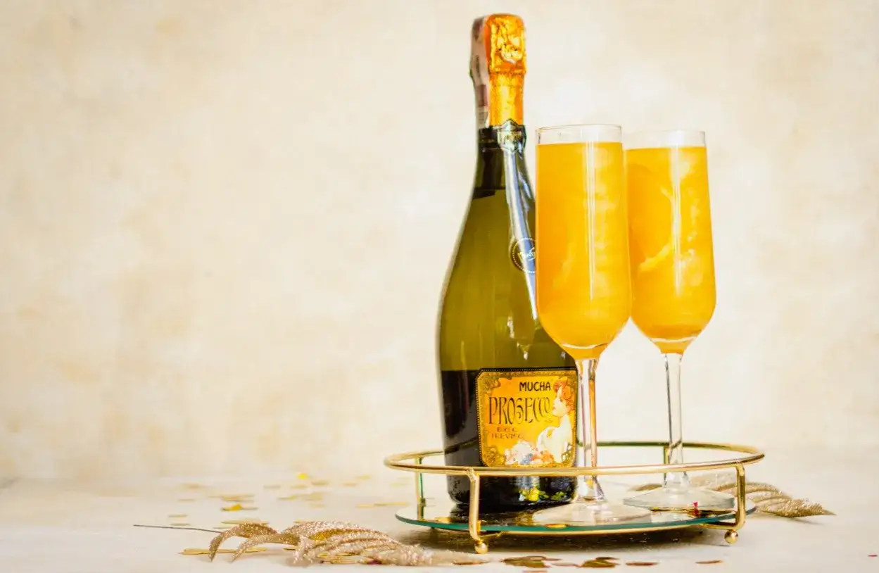 Dwa kieliszki musującego drinka z marakują i butelka prosecco na złotej tacy.