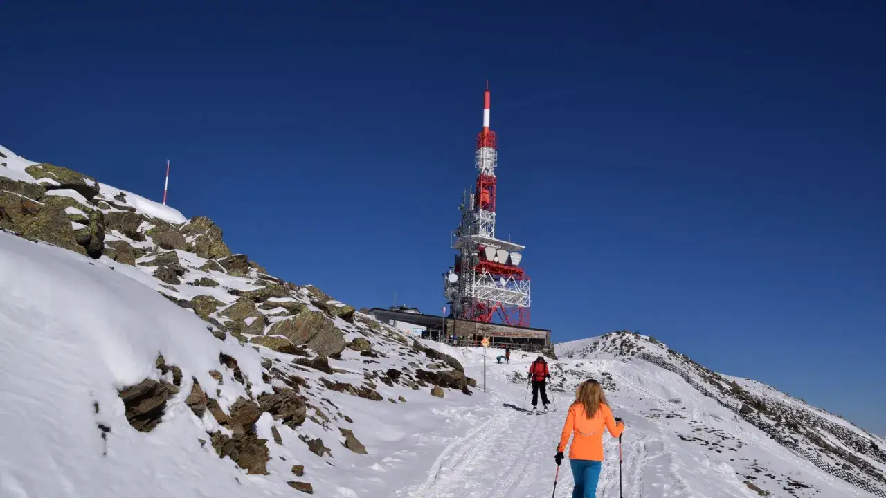 Schneebedeckte Berge bei Innsbruck im Winter. Zwei Skifahrer steigen einen verschneiten Hang hinauf, im Hintergrund ein Sendeturm.