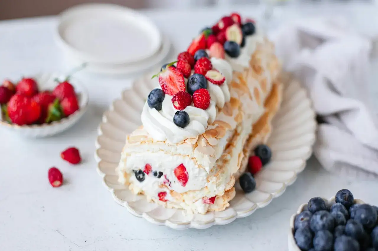 Pyszny tort pavlova z bitą śmietaną i owocami leśnymi, udekorowany truskawkami i borówkami.