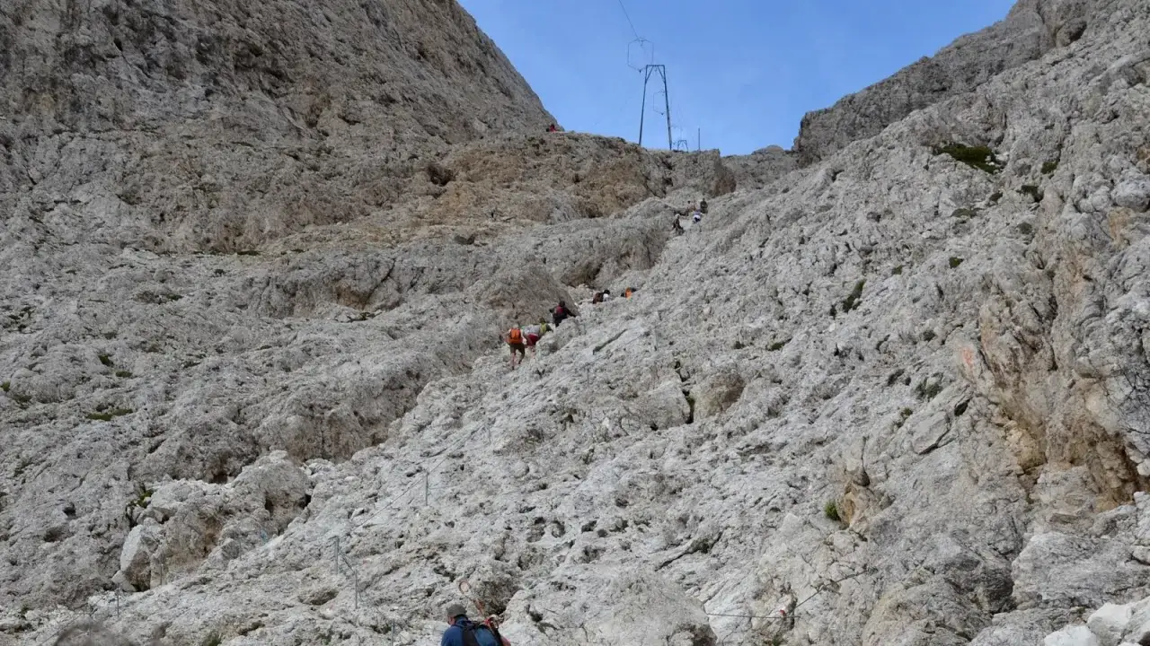 Escursionisti affrontano la **difficolt&agrave;** del sentiero roccioso verso il **Rifugio Re Alberto**. Cavi d'acciaio aiutano la salita.