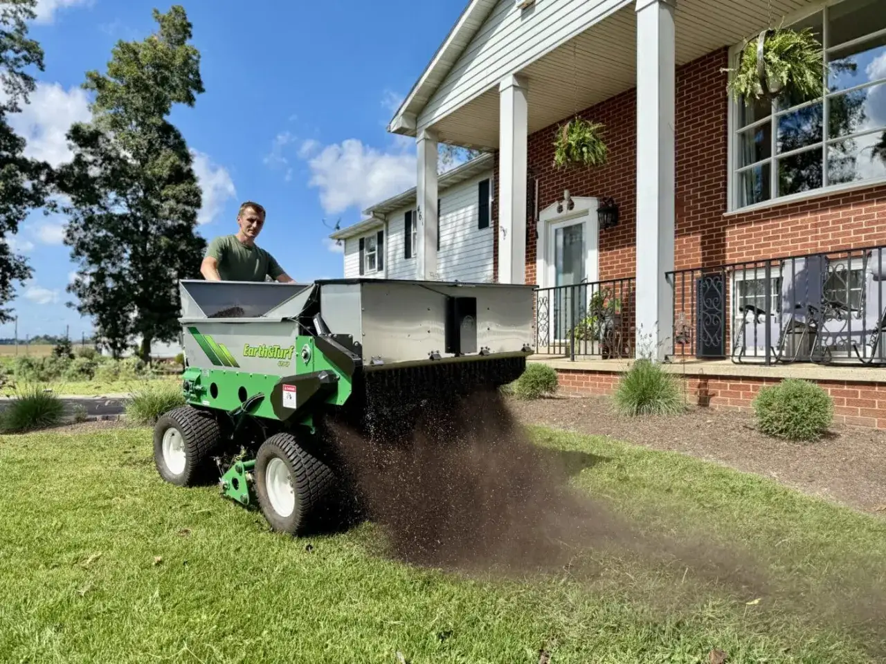 Man using a spreader to apply soil to a lawn, a great way to fix a bumpy lawn and improve its appearance.