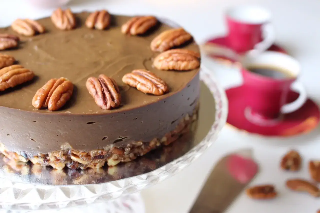 En läcker raw tårta med chokladsmak, toppad med pekannötter. Serveras med kaffe och en spatel.