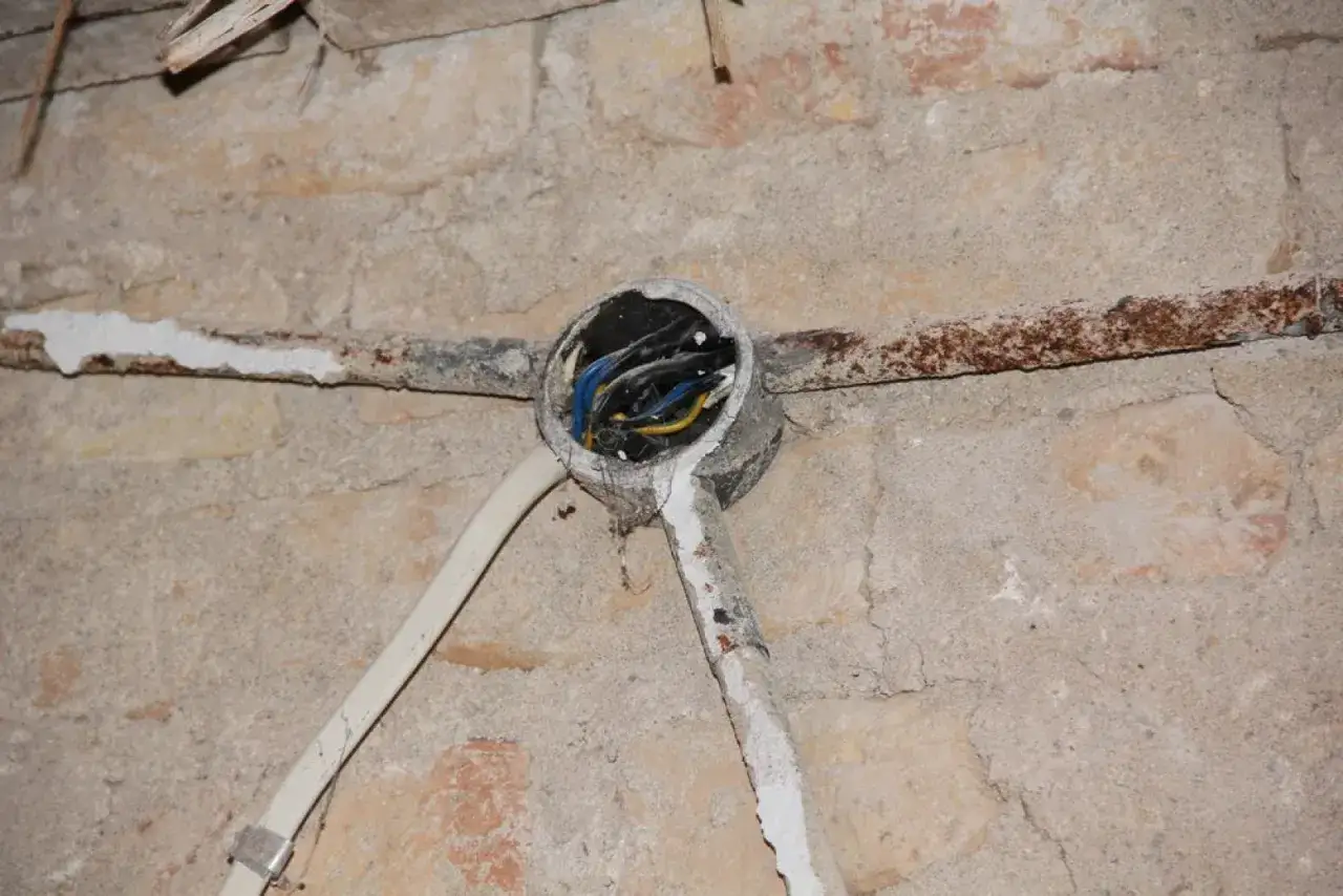 Stara instalacja aluminiowa z widocznymi przewodami w puszce, na tle ceglanej ściany.