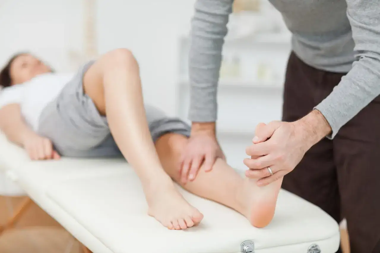 Fizjoterapeuta bada nogę pacjentki, dotykając jej łydki i stopy. Zwraca uwagę na kość piszczelową.