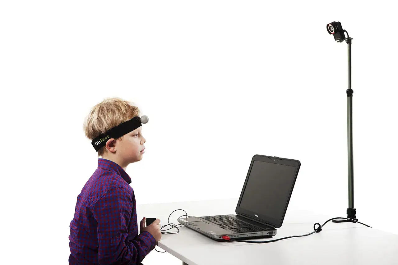 Chłopiec w opasce z czujnikiem bierze udział w teście moxo. Przed nim laptop i kamera na statywie.