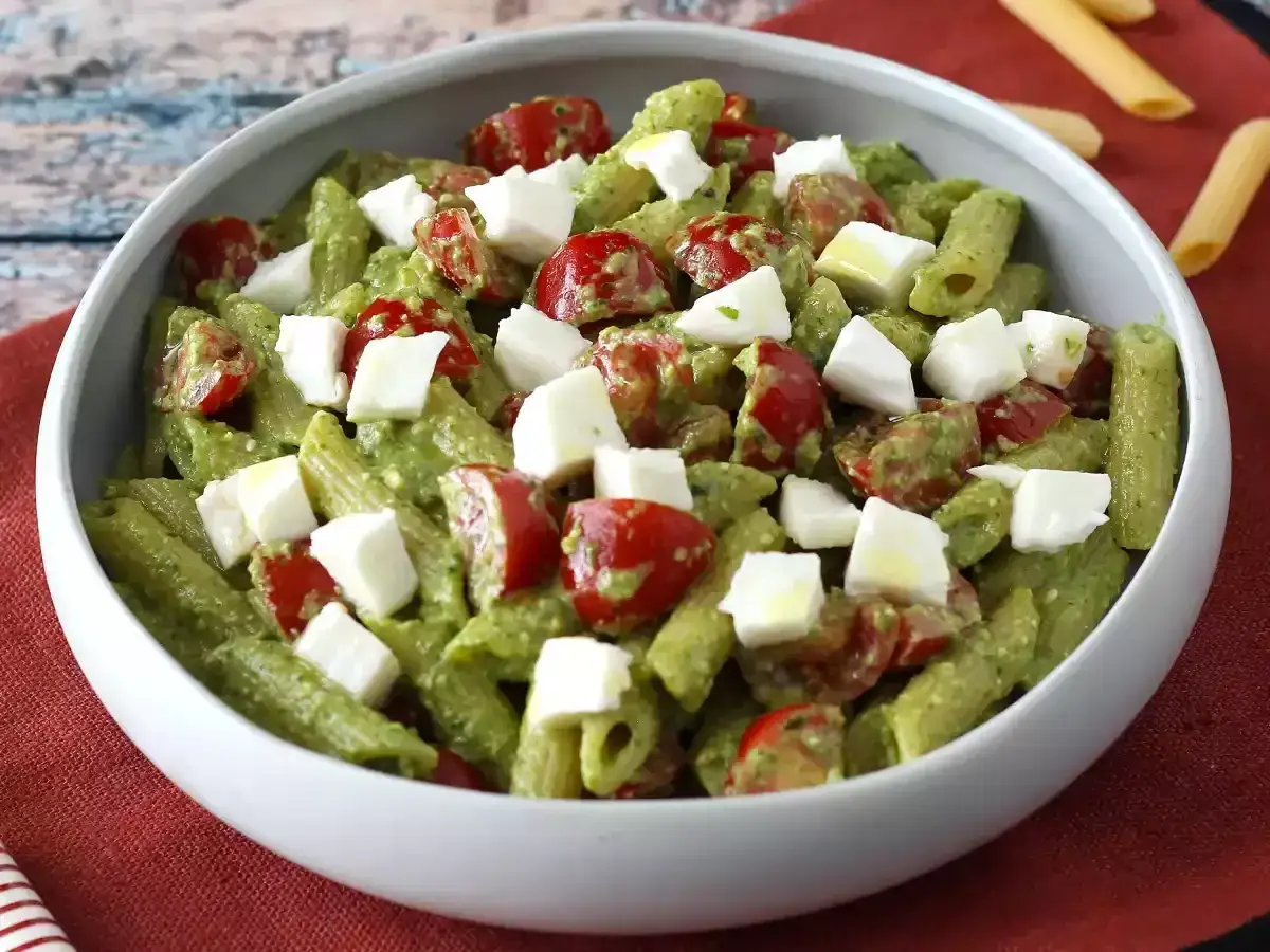 Deliziosa pasta fredda al pesto con pomodorini e cubetti di mozzarella, un piatto estivo perfetto.