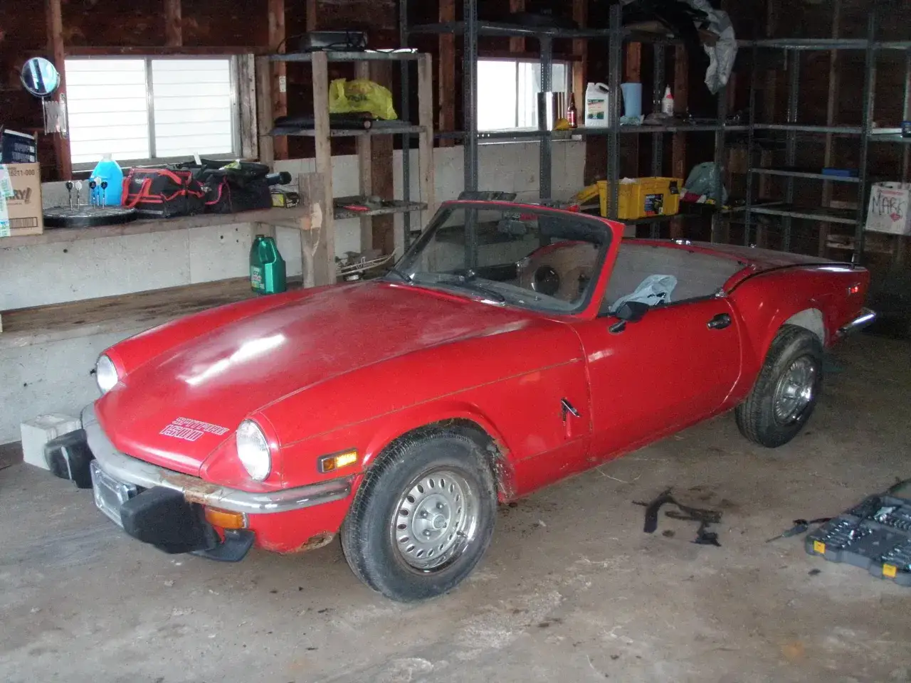 R&ouml;d Triumph Spitfire cabriolet i ett garage, redo f&ouml;r renovering.