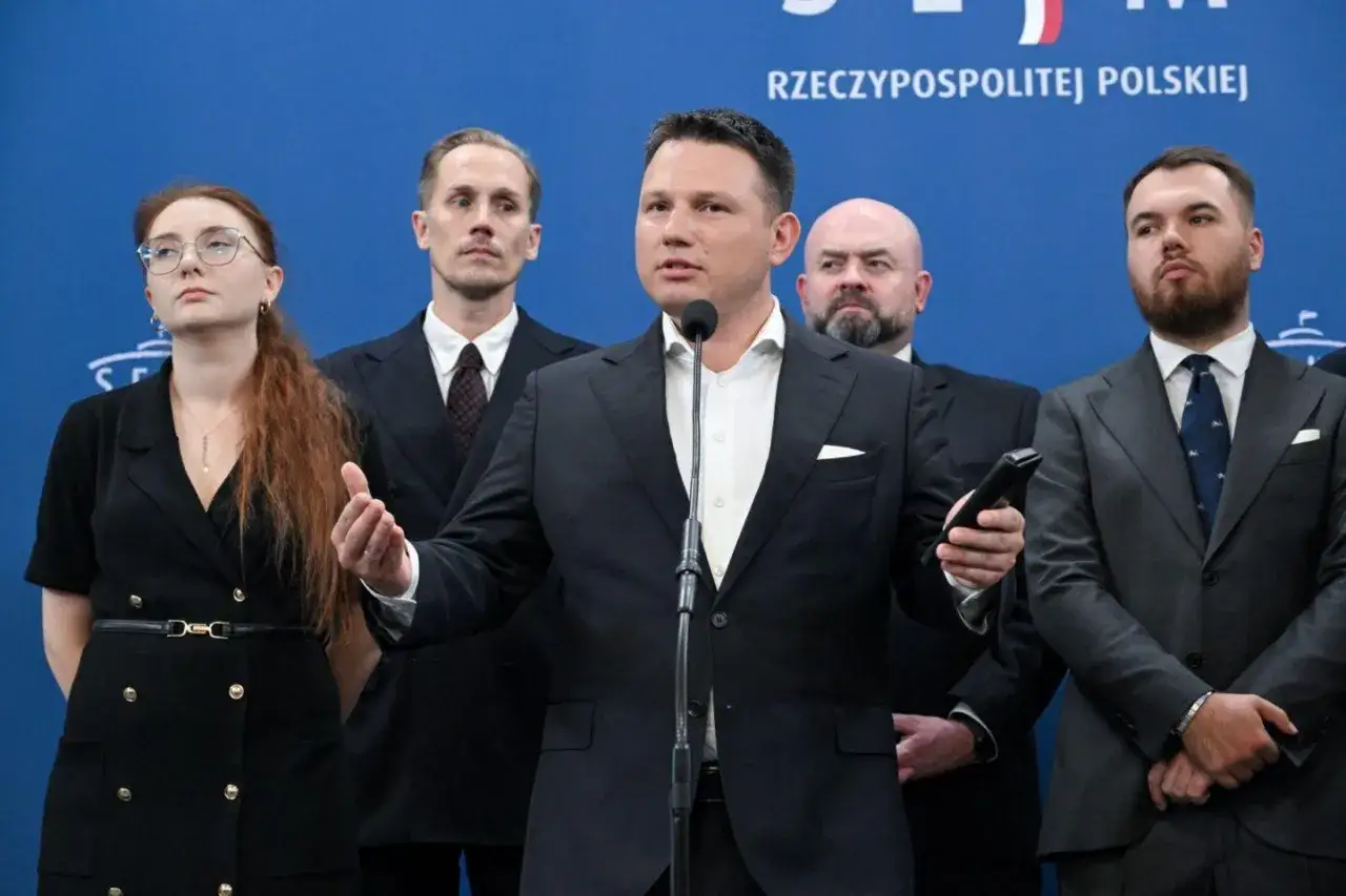 Konfederacja liderzy przemawiający do tłumu. Mężczyzna w garniturze mówi do mikrofonu, otoczony przez innych polityków.