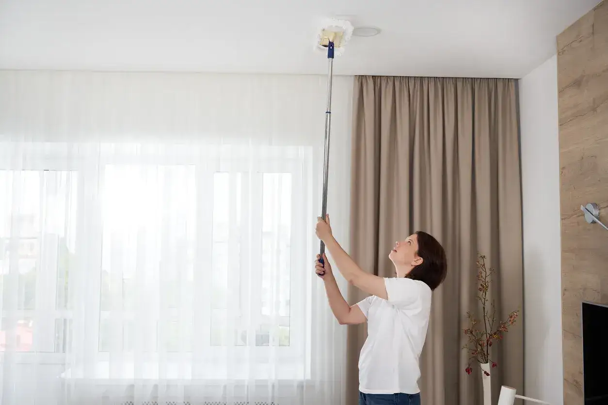 Donna pulisce il soffitto con uno spolverino telescopico, un lavoro che richiede attenzione per la pittura soffitto.