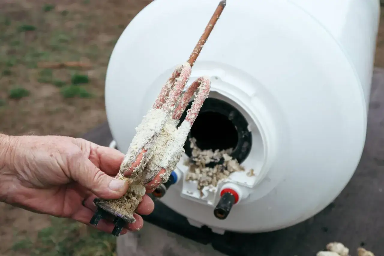 Main d'un homme tenant une r&eacute;sistance de chauffe-eau entartr&eacute;e. Il est temps de detartrer chauffe eau pour un fonctionnement optimal.