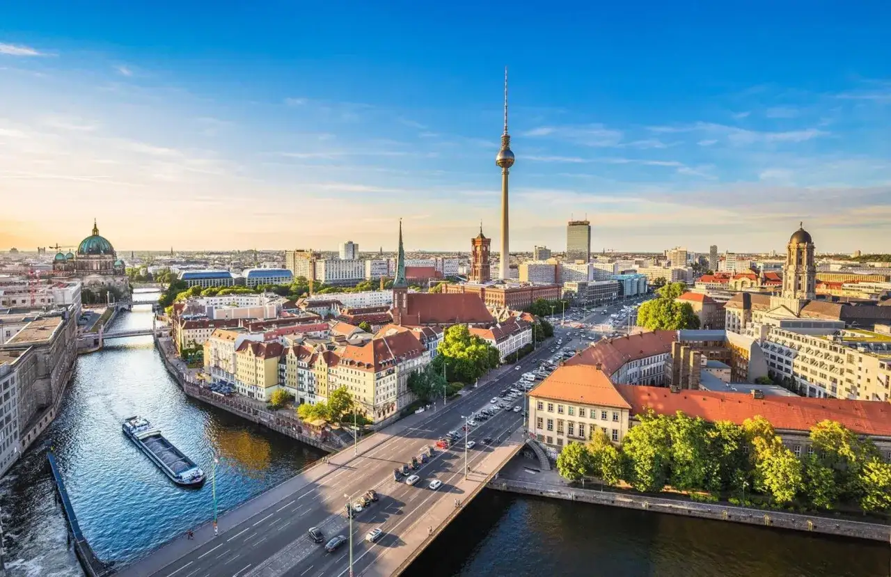 Fakta om Berlin: En solig dag &ouml;ver Berlin med Spree, TV-tornet och Berliner Dom. En b&aring;t passerar under en bro.