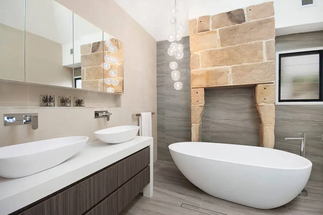 Salle de bain moderne avec baignoire &icirc;lot, double vasque et chemin&eacute;e en pierre. La puissance &eacute;clairage salle de bain est assur&eacute;e par des suspensions lumineuses.