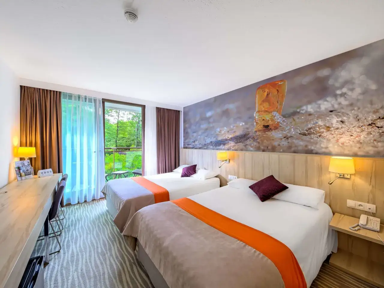 Pokój hotelowy z dwoma łóżkami, widokiem na zieleń i muralem z bursztynem. Idealne miejsce na wypoczynek w **Posejdon Gdańsk**.