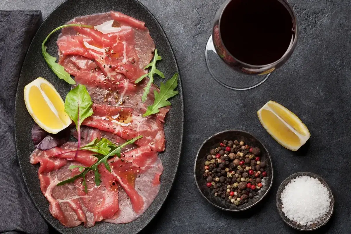 Delicioso carpaccio de ternera con rúcula, limón, pimienta y sal. Acompañado de una copa de vino tinto.